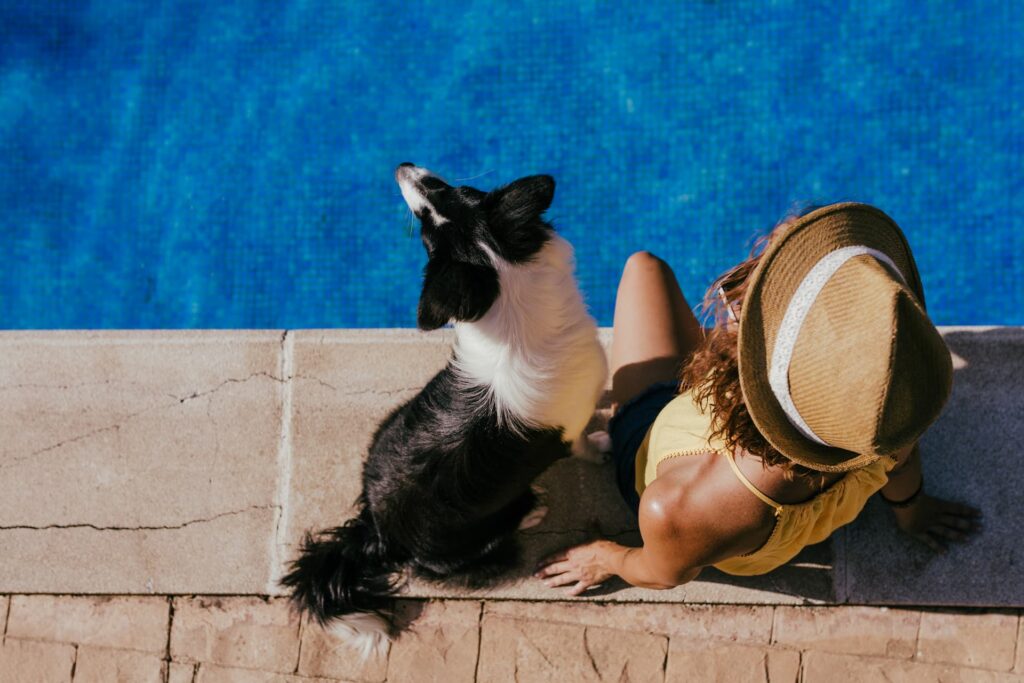 Mulher relaxando à beira da piscina com seu cachorro em hotel pet-friendly, aproveitando o sol e o lazer durante as férias.