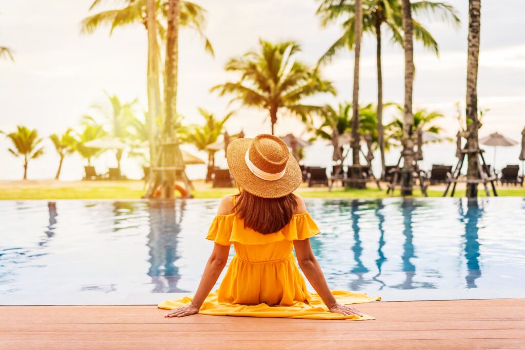 Mulher sentada à beira da piscina observando o mar, representando tranquilidade e liberdade para viajar com o Clube Bancorbrás.