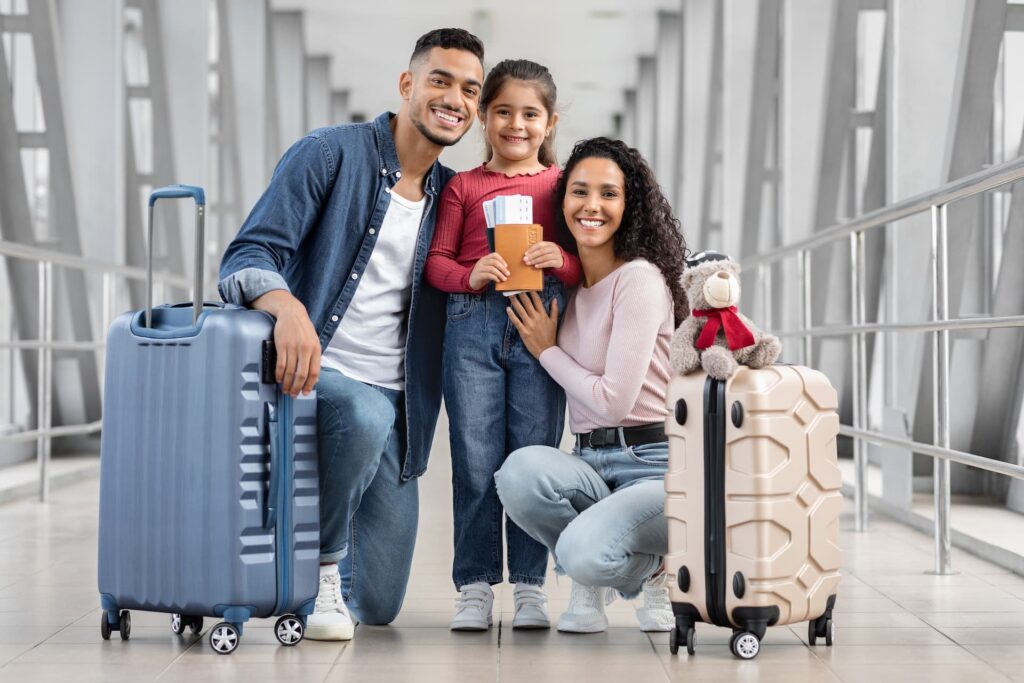 Família sorrindo em um terminal de aeroporto segurando malas e passaportes.