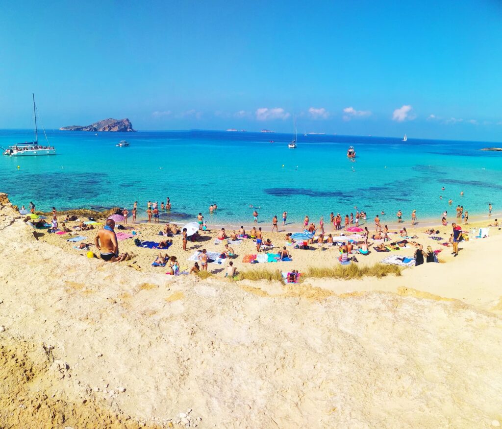 Vista panorâmica da praia de Cala Comte em Ibiza, com águas cristalinas e falésias ao fundo.
