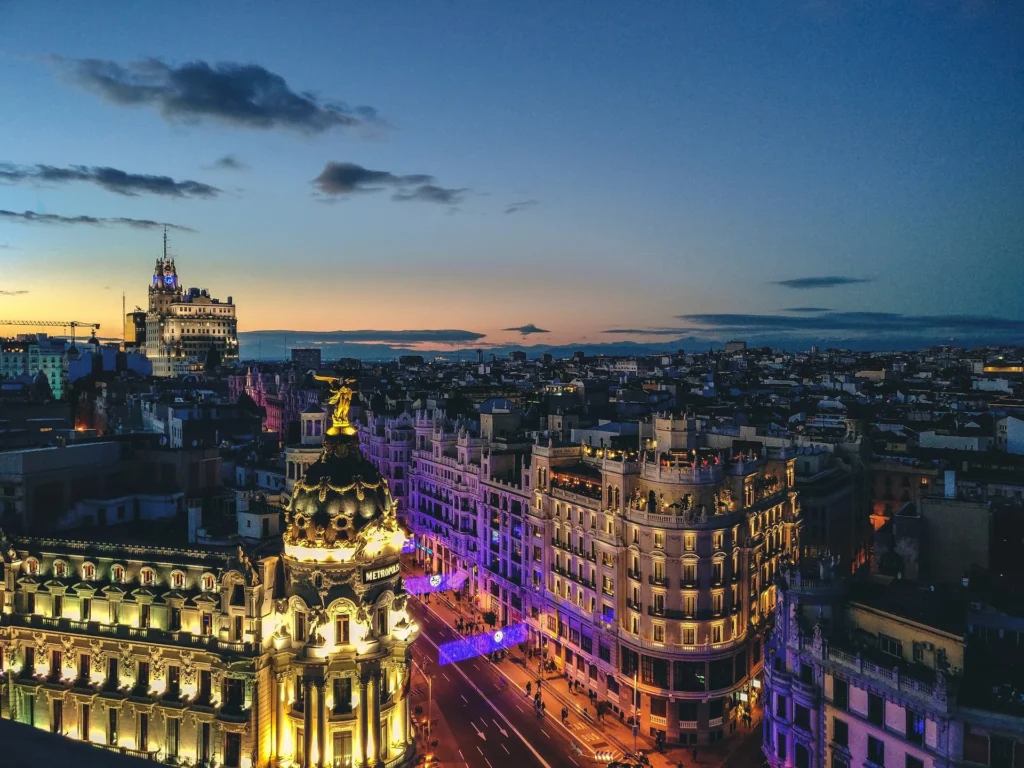 Vista aérea noturna de Madri com as luzes da cidade e prédios históricos iluminados sob o céu escuro.