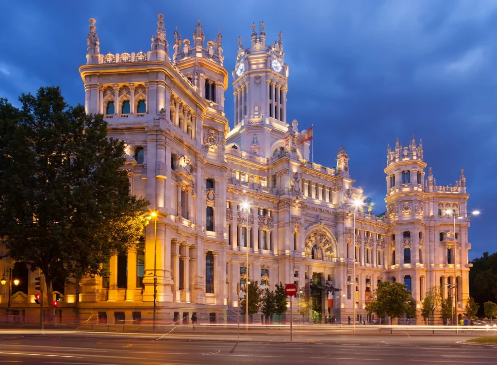 Vista do Palácio da Comunicação em Madri sob a luz do crepúsculo de verão, destacando a arquitetura iluminada.