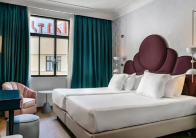 Quarto elegante com duas camas de solteiro juntas, cabeceira bordô estilizada e cortinas verdes escuras em madri.