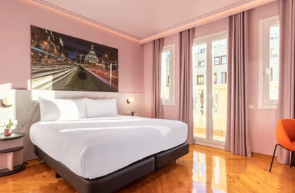 Quarto de hotel contemporâneo com cama de casal, paredes em tom rosa claro e um quadro grande da cidade de Madri na parede.