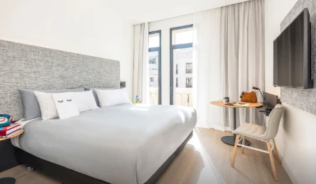 Quarto de estilo moderno com cama grande, decoração em tons de cinza e mesa de trabalho próxima à janela em madri.