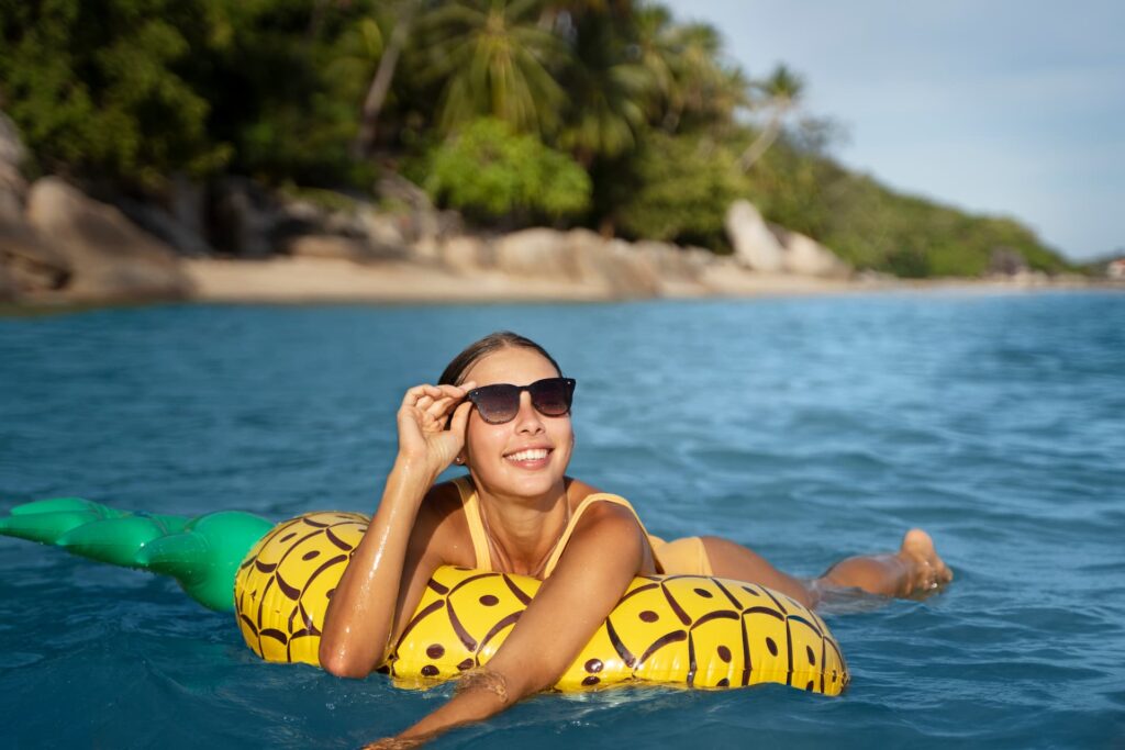 Vista frontal de uma mulher sorridente deitada em um flutuador inflável de abacaxi em águas calmas e cristalinas de uma praia de rio.