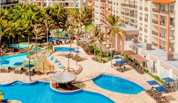 Vista aérea de um complexo de piscinas azuis rodeado por coqueiros e prédios do resort.